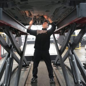 man-in-black-jacket-and-black-pants-standing-under-vehicle-3807811